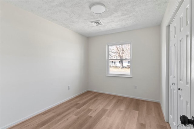 unfurnished bedroom featuring visible vents, a textured ceiling, a closet, light wood finished floors, and baseboards