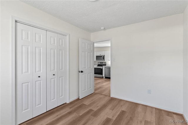 unfurnished bedroom with light wood finished floors, baseboards, a textured ceiling, and a closet