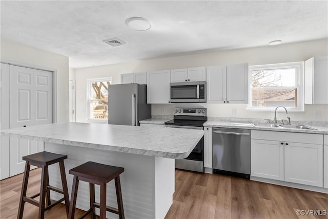 kitchen featuring visible vents, a kitchen bar, wood finished floors, stainless steel appliances, and a sink