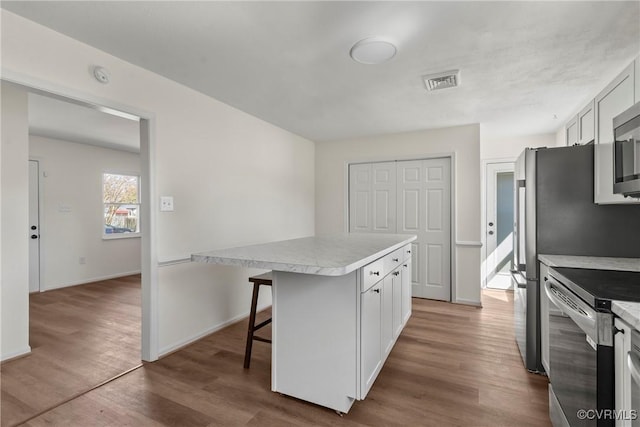 kitchen with visible vents, electric stove, a kitchen island, wood finished floors, and light countertops