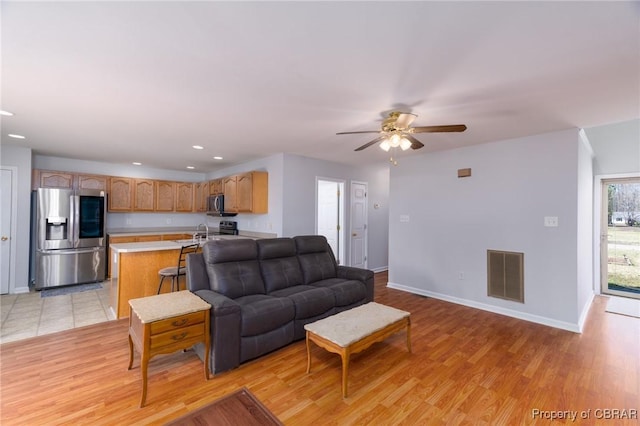 living room featuring a ceiling fan, visible vents, baseboards, light wood-style flooring, and recessed lighting