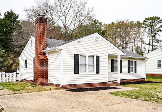 view of front of house featuring a shingled roof, a chimney, a front yard, and fence