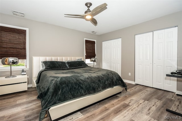 bedroom with visible vents, baseboards, two closets, and wood finished floors