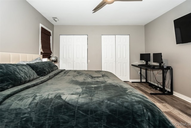 bedroom featuring visible vents, two closets, baseboards, wood finished floors, and a ceiling fan