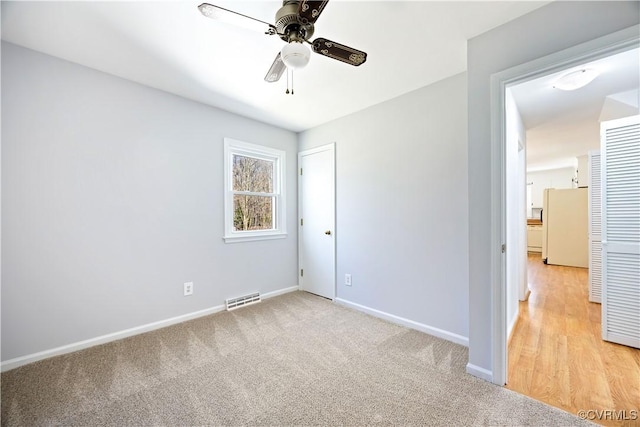 unfurnished bedroom featuring visible vents, baseboards, light colored carpet, freestanding refrigerator, and a ceiling fan