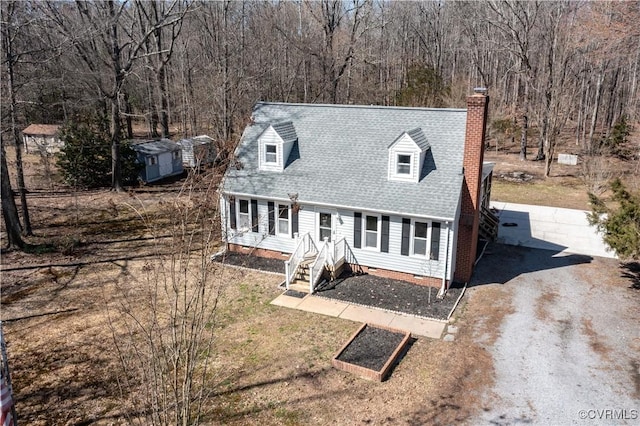 new england style home with a chimney, crawl space, a wooded view, and a shingled roof