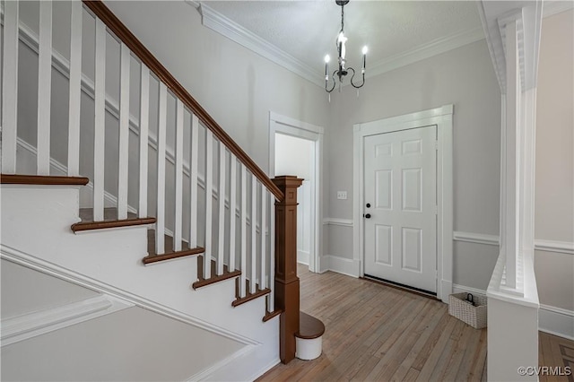 foyer entrance featuring stairway, wood finished floors, crown molding, and a chandelier