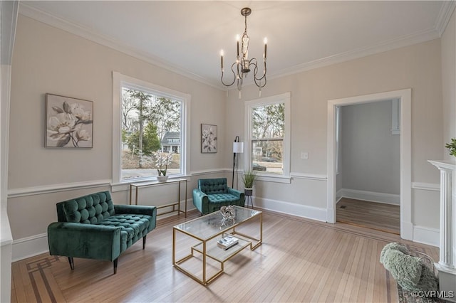 living area with a chandelier, crown molding, baseboards, and wood finished floors