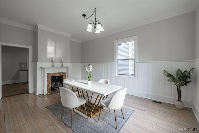 dining room featuring light wood-type flooring, a notable chandelier, wainscoting, and a high end fireplace