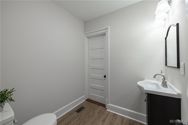 half bathroom featuring visible vents, baseboards, toilet, wood finished floors, and vanity