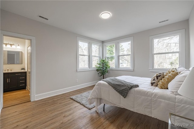 bedroom with visible vents, light wood-style flooring, ensuite bathroom, and baseboards