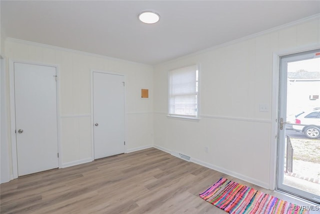 empty room with visible vents, plenty of natural light, light wood-type flooring, and ornamental molding