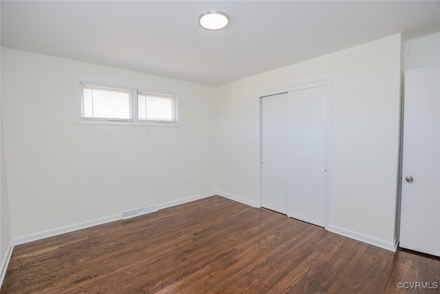 unfurnished bedroom featuring a closet, visible vents, dark wood-type flooring, and baseboards