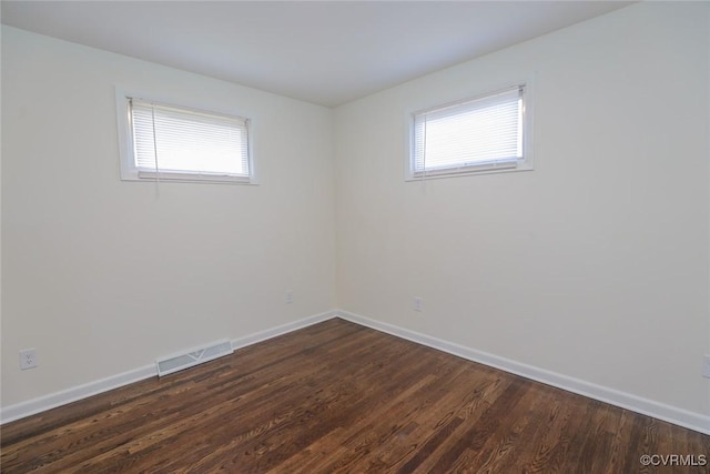 empty room featuring baseboards, visible vents, and dark wood-style flooring