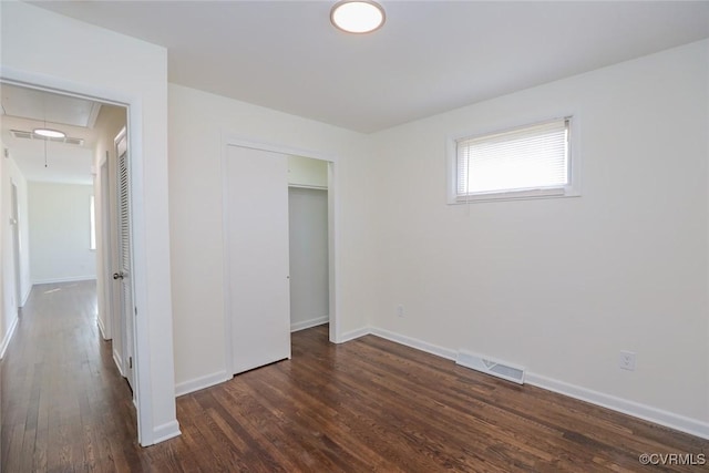 unfurnished bedroom featuring wood finished floors, visible vents, baseboards, attic access, and a closet