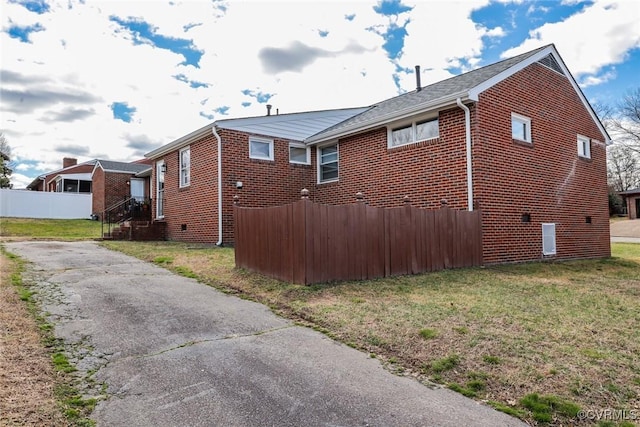 view of side of property with aphalt driveway, a yard, fence, and brick siding