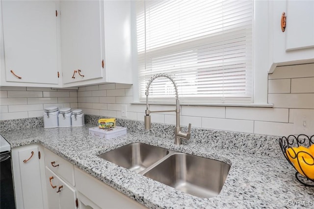 kitchen with a sink, light stone countertops, tasteful backsplash, and white cabinets