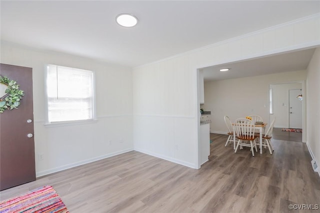 foyer entrance featuring baseboards, crown molding, and light wood finished floors