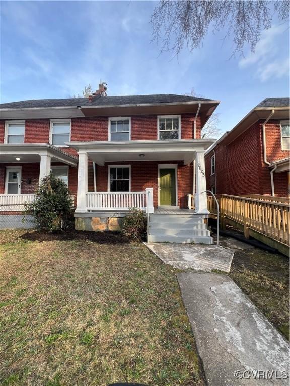 view of front of home with a porch, brick siding, and a front yard