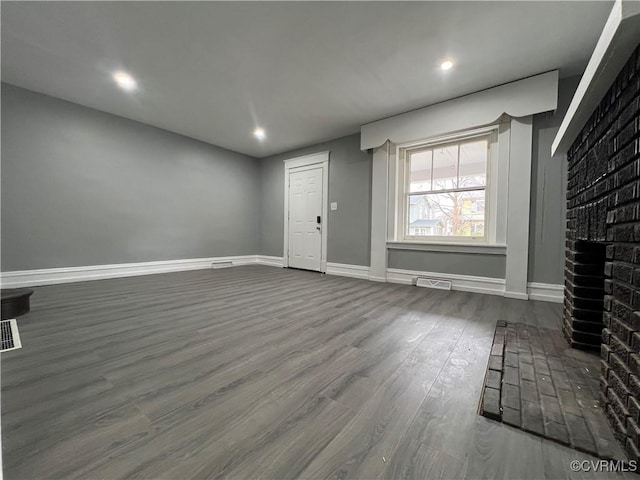 unfurnished living room with baseboards, visible vents, dark wood finished floors, recessed lighting, and a brick fireplace