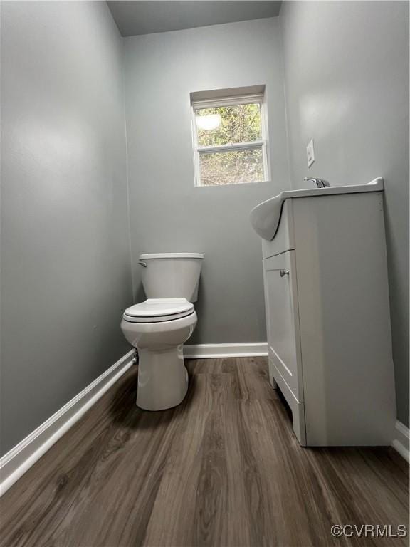 half bath with toilet, wood finished floors, and baseboards