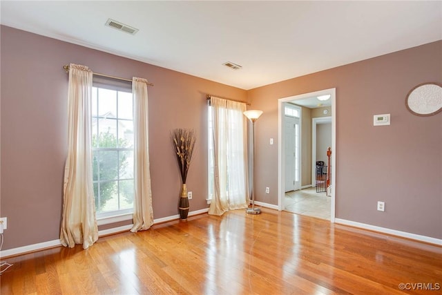 empty room featuring visible vents, plenty of natural light, and wood finished floors