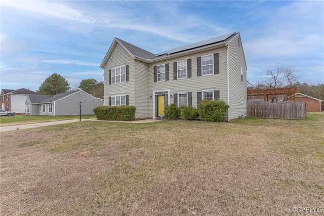 colonial-style house with driveway, solar panels, a front yard, and fence