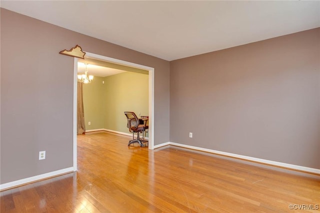 spare room with an inviting chandelier, baseboards, and light wood-style floors