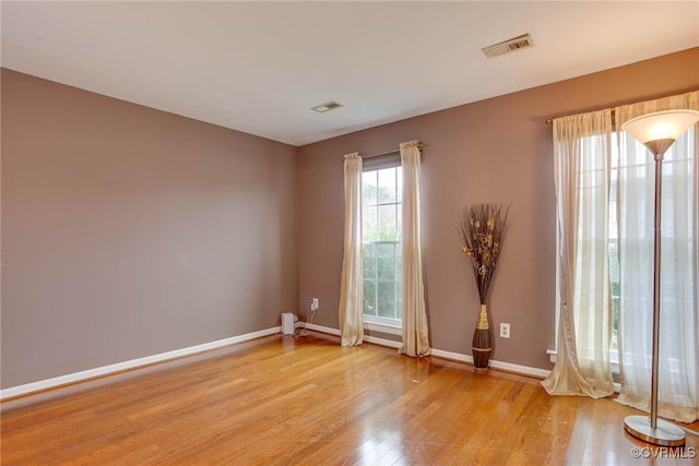 spare room featuring light wood finished floors, visible vents, and baseboards