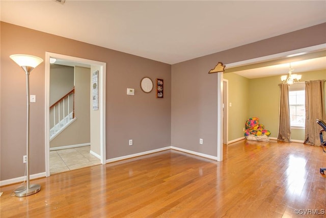 empty room featuring baseboards, a chandelier, stairs, and light wood finished floors