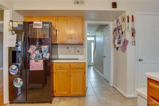 kitchen with visible vents, light countertops, light tile patterned floors, decorative backsplash, and black refrigerator with ice dispenser