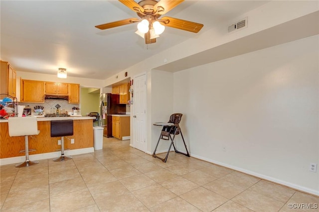 kitchen with visible vents, under cabinet range hood, freestanding refrigerator, a peninsula, and light countertops