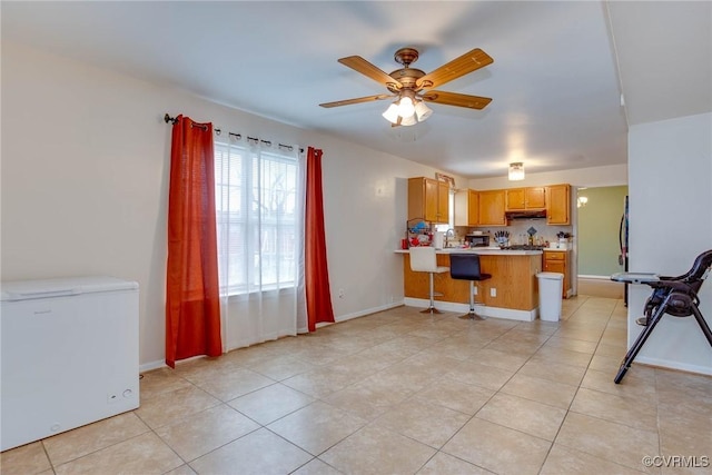 kitchen with a peninsula, ceiling fan, white fridge, light countertops, and under cabinet range hood