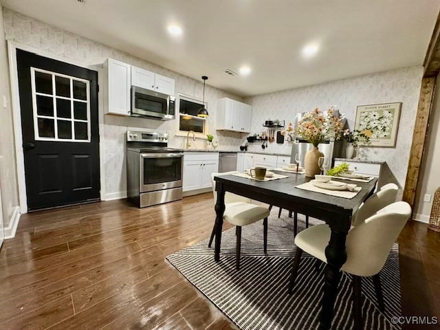 kitchen featuring wallpapered walls, dark wood-type flooring, light countertops, appliances with stainless steel finishes, and white cabinetry