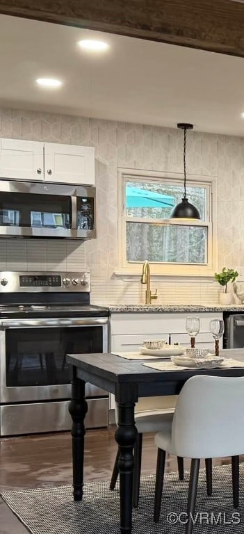 room details with wood finished floors, a sink, appliances with stainless steel finishes, white cabinetry, and decorative light fixtures