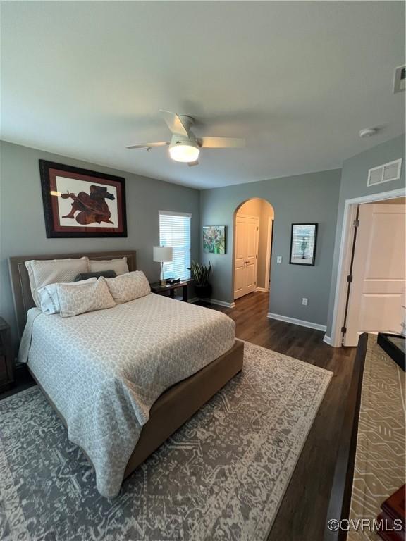 bedroom with visible vents, a ceiling fan, arched walkways, baseboards, and dark wood-style flooring