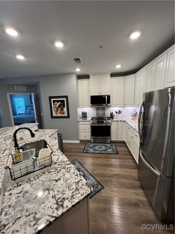 kitchen with visible vents, appliances with stainless steel finishes, dark wood-style flooring, and light stone countertops