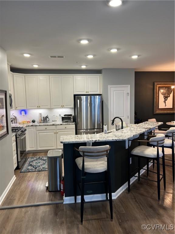 kitchen featuring visible vents, a kitchen bar, dark wood-type flooring, freestanding refrigerator, and black range with gas cooktop