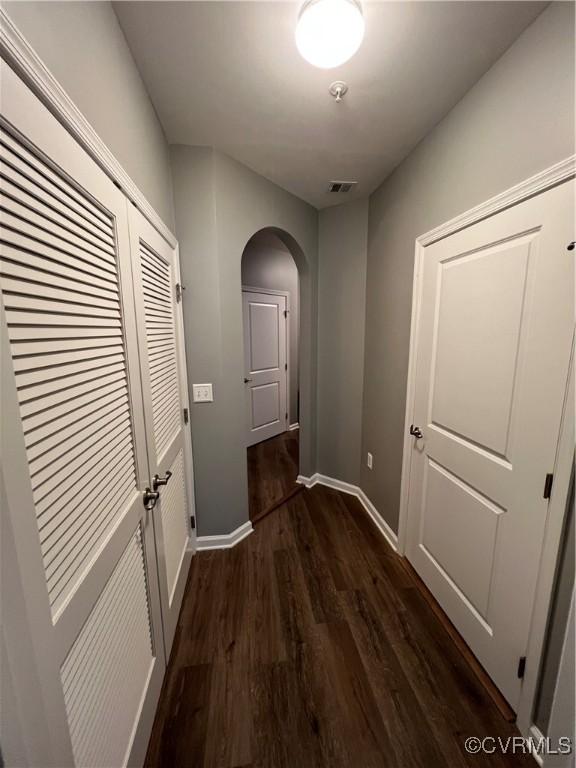 corridor with dark wood-type flooring, arched walkways, visible vents, and baseboards