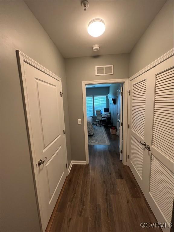 hallway featuring dark wood finished floors, baseboards, and visible vents