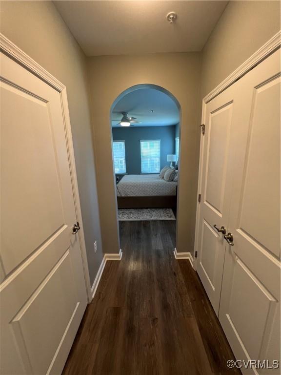 hallway with baseboards, dark wood-style flooring, and arched walkways