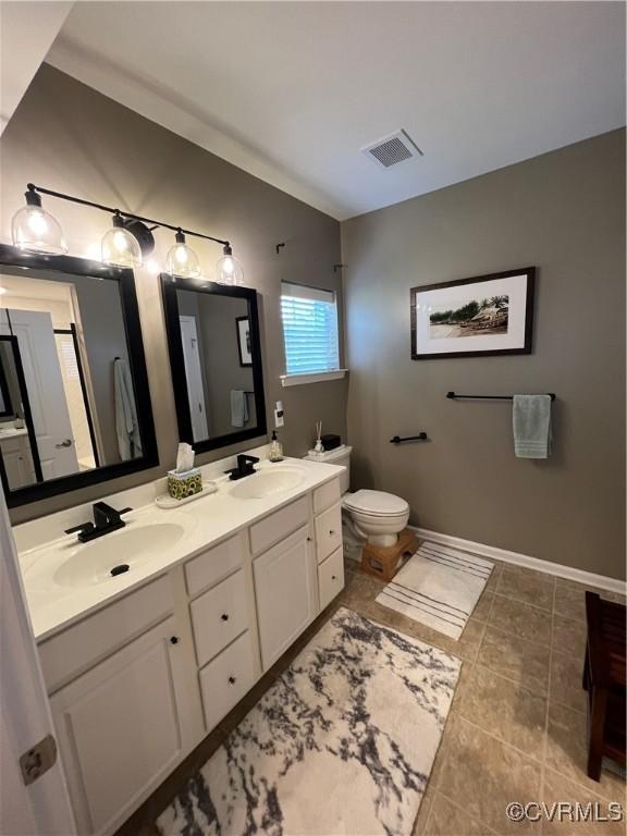 bathroom with double vanity, toilet, visible vents, and a sink