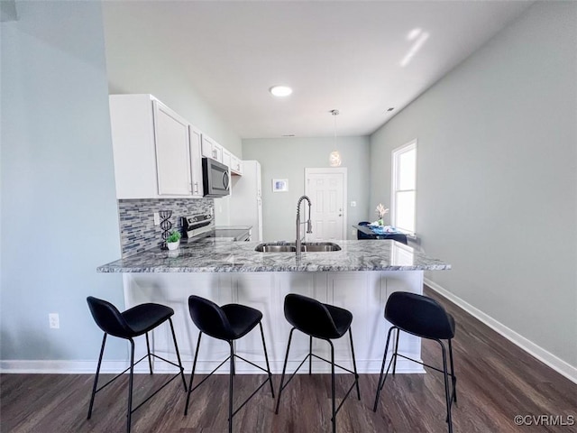 kitchen with a sink, backsplash, stainless steel appliances, a peninsula, and white cabinets