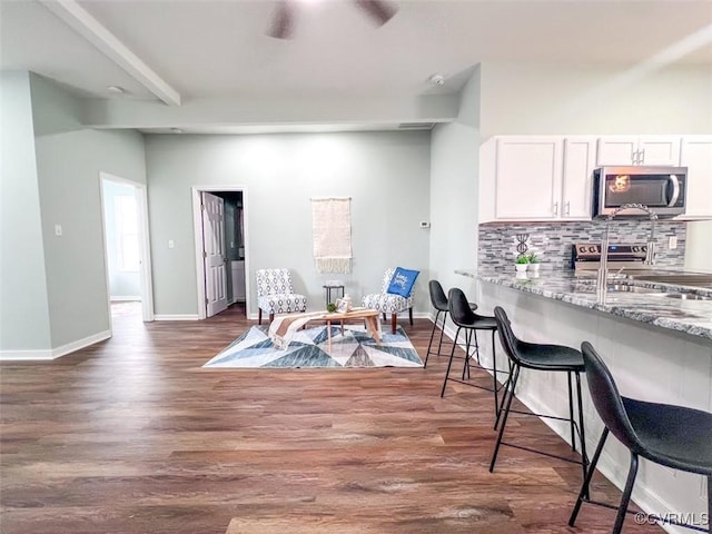 kitchen featuring wood finished floors, beam ceiling, stainless steel appliances, a kitchen breakfast bar, and backsplash