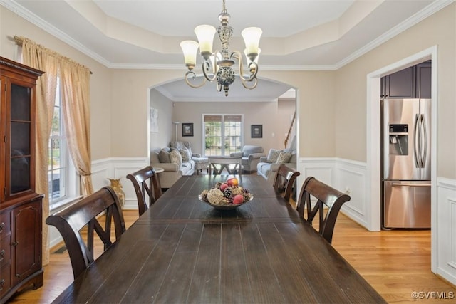 dining space featuring light wood-style flooring, a chandelier, arched walkways, a tray ceiling, and wainscoting