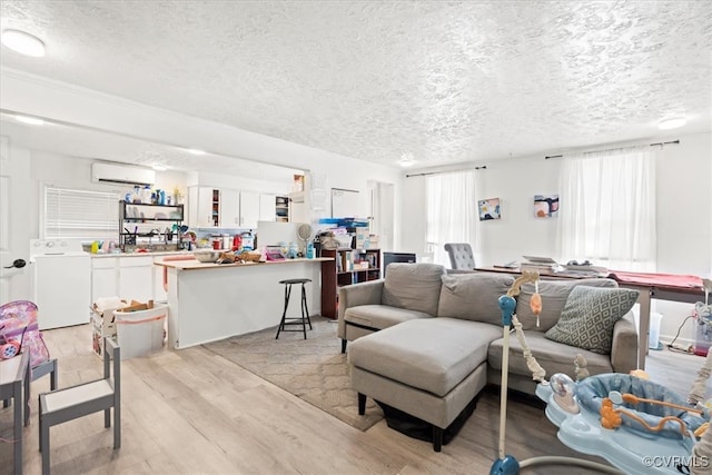 living area with a wall unit AC, washer / clothes dryer, light wood finished floors, and a textured ceiling