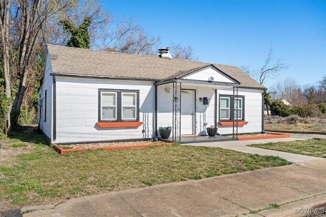 bungalow featuring a chimney, a front yard, and a shingled roof