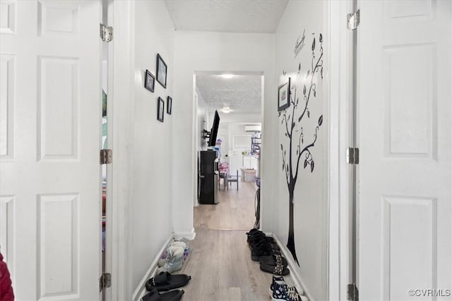 hall featuring light wood-style flooring, a textured ceiling, and baseboards