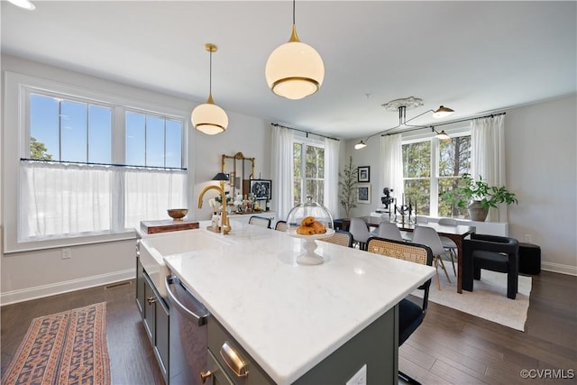 kitchen featuring a sink, decorative light fixtures, light countertops, a kitchen breakfast bar, and stainless steel dishwasher