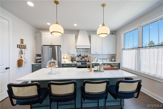 kitchen with a center island with sink, a breakfast bar, stainless steel appliances, custom range hood, and backsplash